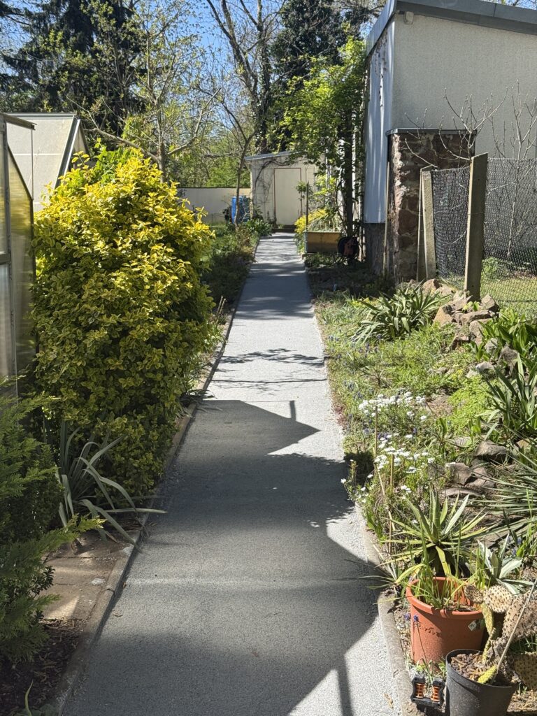 Die graue Wegedecke integriert sich harmonisch in die bestehenden Staudenbeete und schafft ein natürliches, ruhiges Gesamtbild des Gartens, Quelle: UrbanGardens GmbH