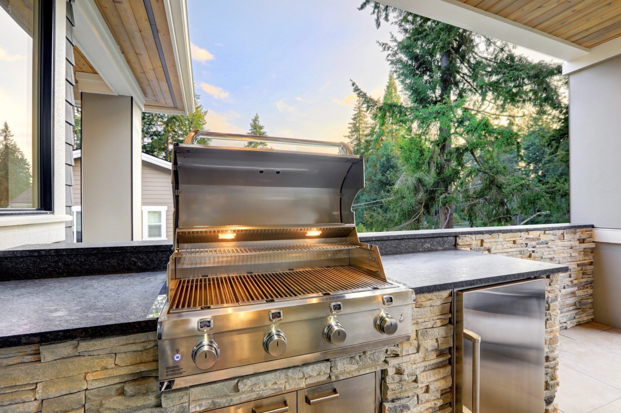 Eleganter Grill auf einer Terrasse mit Blick auf grüne Bäume im Hintergrund.